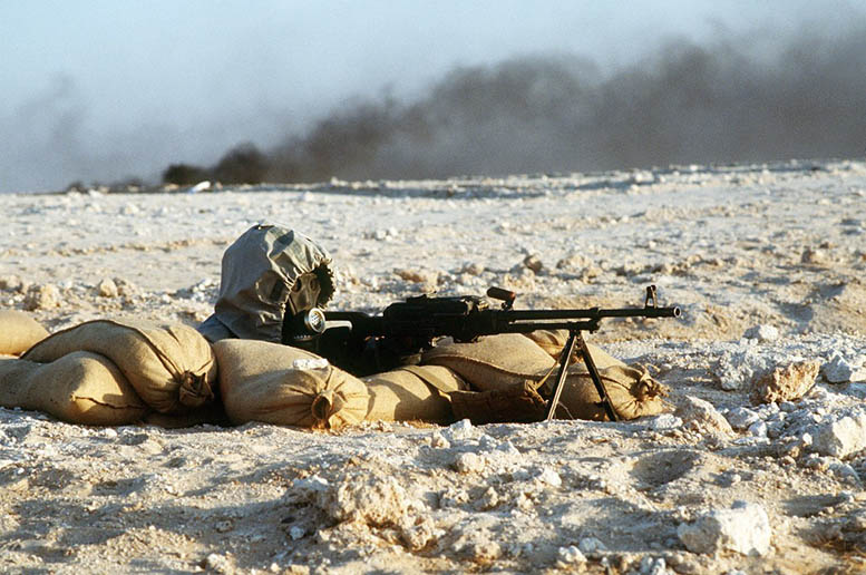 A Syrian soldier aims a 7.62mm PKM light machine gun from his position in a foxhole during a firepower demonstration, part of Operation Desert Shield. The soldier is wearing a nuclear-biological-chemical warfare mask