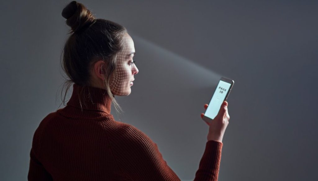 Female scans face using facial recognition system on smartphone for biometric identification. Future high tech technology and face id
