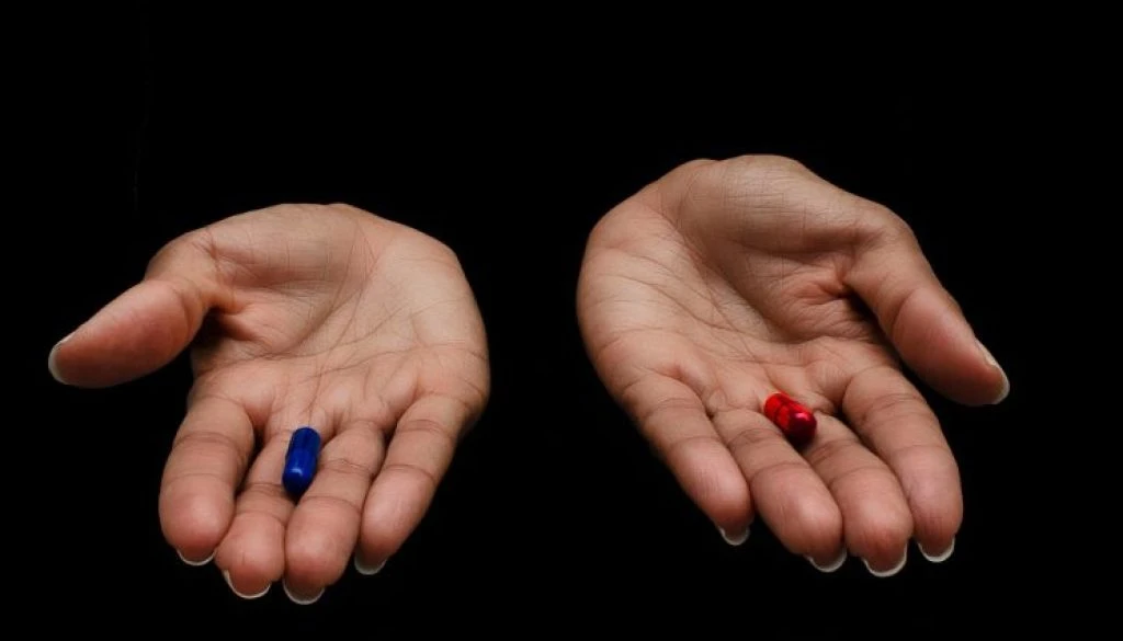 Hands of a black woman offering the red and the blue pills on a black background. Concept of ugly truth vs beautiful lie, reality vs fiction.