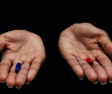 Hands of a black woman offering the red and the blue pills on a black background. Concept of ugly truth vs beautiful lie, reality vs fiction.