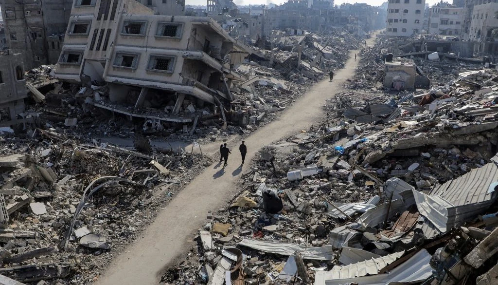 Palestinians walk past destroyed houses, in Jabalia refugee camp