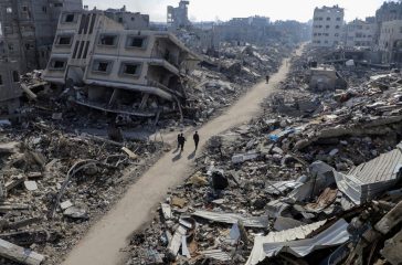 Palestinians walk past destroyed houses, in Jabalia refugee camp