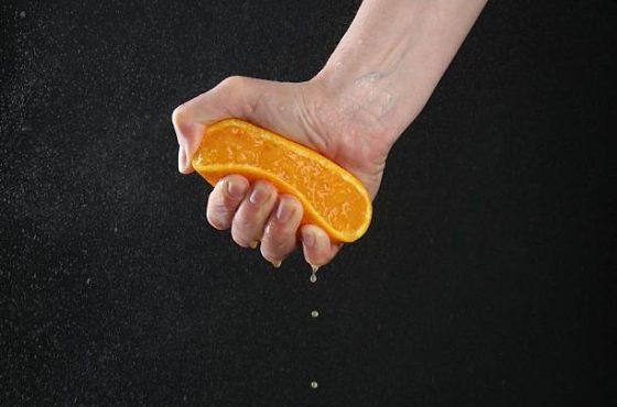 Woman squeezing orange on black background, closeup